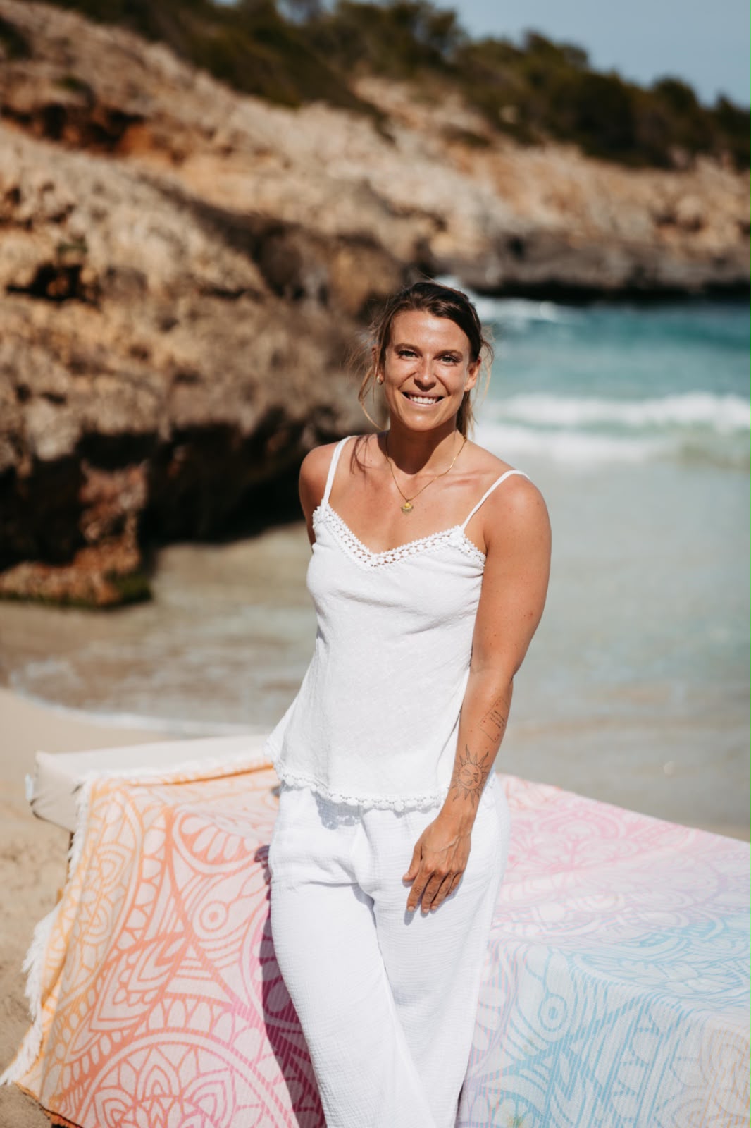 Melissa steht lächelnd in Weiß vor ihrer Massageliege an einem Strand auf Mallorca