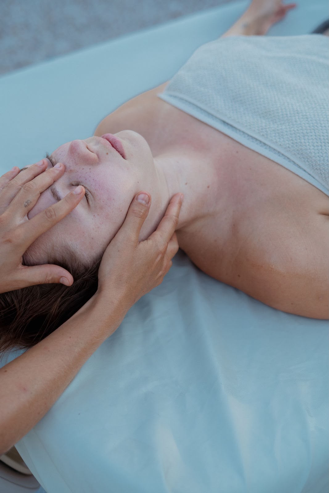 Sanfte Kopf- und Gesichtsmassage bei einer liegenden Kundin mit Handtuch